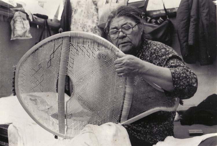 Sarah Bosum of Mistassini lacing the midsection of a man's beavertail snowshoe with caribou skin. The loose end of the string is held in the mouth to maintain tension on the weave , Lac Capichigamau , Quebec 1985; photo Henri Vaillancourt  