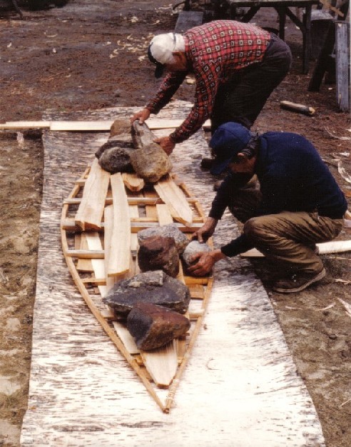 Laying out a sheet of bark for a new birchbark canoe . The gunnels are weighted on the birchbark sheet ...the bark is  then bent up along the sides into the shape of the canoe ; from ''Building an Algonquin Birchbark Canoe '' ; photo Henri Vaillancourt ; Maniwaki, Quebec , 1980