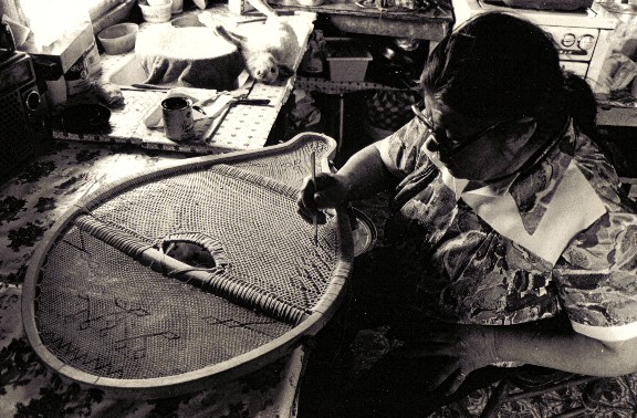 Sarah Bosum  painting the woven designs of beavertail snowshoes to highlight the pattern . Paint is also used as  dots , or groups of dots , on the toe crossbar as well  as around the edge of the center weave ;lines are sometimes also painted on the frame at the toe and tail of the snowshoe . These decorations are traditional in the Quebec - Labrador area  , and can be seen in many very old snowshoes  preserved in museum collections .Assinica Lake 1980 ; photo Henri Vaillancourt