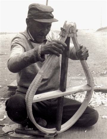 Mathieu Mestenapeo of La Romaine, Quebec examining a newly bent pair of beavertail snowshoes . These frames are bent with an exceptionally  tight rounded tail....just one of the many variant patterns of beavertail snowshoes in the Quebec- Labrador area  ; photo 1978, Henri Vaillancourt